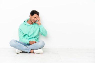 Beyaz tenli yakışıklı adam yerde oturmuş gülüyor.