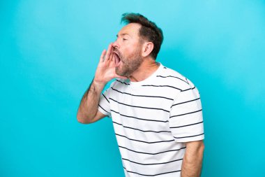 Mavi arka planda izole edilmiş orta yaşlı beyaz adam ağzı sonuna kadar açık bağırıyor.