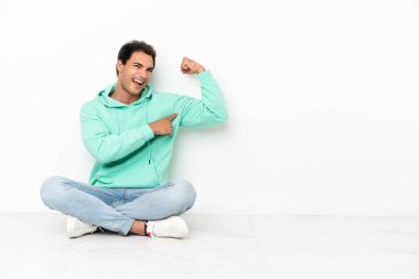 Beyaz, yakışıklı bir adam yerde oturmuş güçlü bir jest yapıyor.