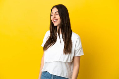 Sarı arka planda izole edilmiş genç beyaz kadın yana bakıyor ve gülümsüyor.