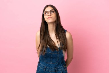 Genç beyaz kadın pembe arka planda izole edilmiş ve yukarı bakıyor.