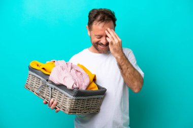 Mavi arka planda izole edilmiş çamaşır sepetini tutan orta yaşlı kadın gülüyor.