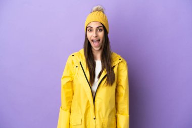 Young caucasian woman wearing a rainproof coat isolated on purple background with surprise facial expression