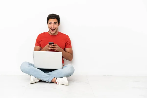 Homem Bonito Caucasiano Com Laptop Sentado Chão Surpreso Enviando Uma — Fotografia de Stock