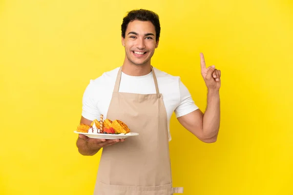 Restaurantkellner Hält Waffeln Vor Isoliertem Gelben Hintergrund Und Weist Auf — Stockfoto