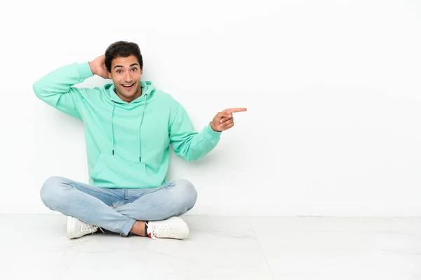 Caucasian Handsome Man Sitting Floor Surprised Pointing Finger Side — Stok fotoğraf
