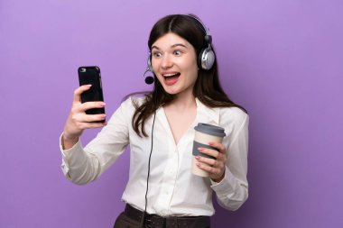 Telemarketer Russian woman working with a headset isolated on purple background holding coffee to take away and a mobile