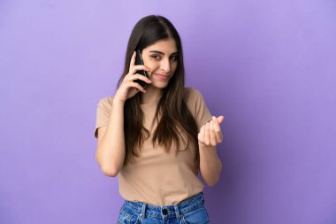 Mor arka planda izole edilmiş cep telefonu kullanan beyaz bir kadın para hareketi yapıyor.