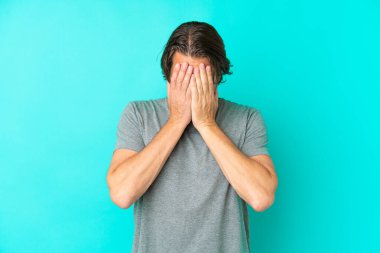 Yaşlı Hollandalı adam yorgun ve hasta bir ifadeyle mavi arka planda izole edilmiş.