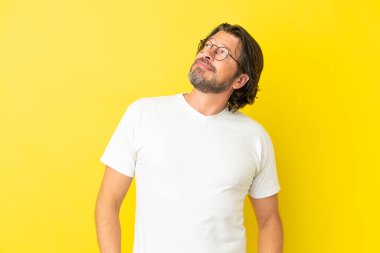 Kıdemli Hollandalı adam sarı arka planda izole edilmiş bir şekilde bakarken bir fikir düşünüyor.