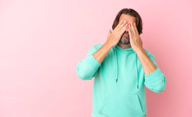 Üst düzey Hollandalı, pembe arka planda izole edilmiş, gözleri elleriyle kapatıyor.