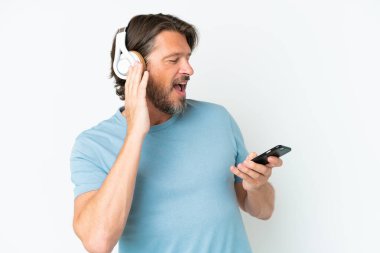 Üst düzey Hollandalı beyaz arka planda izole edilmiş. Cep telefonuyla müzik dinliyor ve şarkı söylüyor.