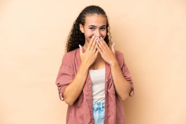Young woman isolated on beige background happy and smiling covering mouth with hands
