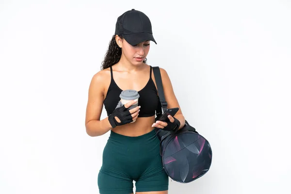 Young sport woman with sport bag isolated on white background holding coffee to take away and a mobile