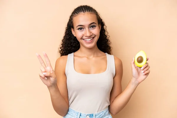 Young Woman Holding Avocado Isolated Beige Background Smiling Showing Victory — Stock Fotó