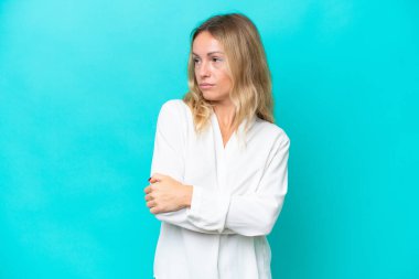 Mavi arka planda izole edilmiş genç Rus kadın kollarını çapraz tutuyor.