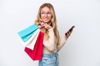 Young Russian woman isolated on white background holding shopping bags and a mobile phone