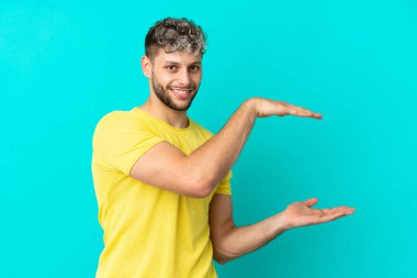 Mavi arka planda izole edilmiş yakışıklı beyaz adam bir ilan vermek için kopyalama alanı tutuyor.