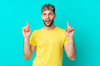 Mavi arka planda izole edilmiş yakışıklı beyaz adam şaşırmış ve yukarı bakıyor.