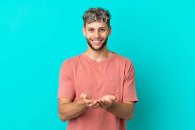 Mavi arka planda izole edilmiş yakışıklı beyaz adam bir ilan vermek için fotokopi makinesini avucunun içinde tutuyor.