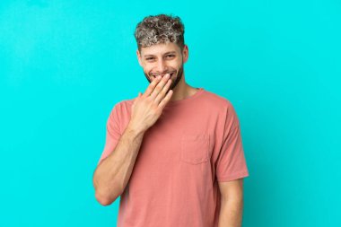Mavi arka planda izole edilmiş yakışıklı beyaz adam mutlu ve gülümsüyor.