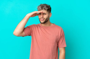 Mavi arka planda izole edilmiş yakışıklı beyaz bir adam. Bir şeye bakmak için uzaklara bakıyor.