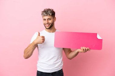 Pembe arka planda izole edilmiş beyaz bir adam boş bir levhayı başparmağıyla tutuyor.