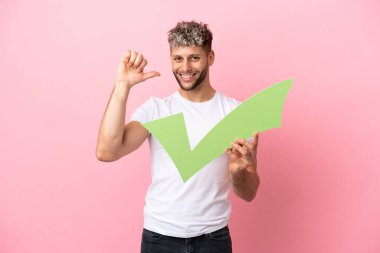 Pembe arka planda izole edilmiş yakışıklı beyaz bir adam elinde gururlu bir jestle bir çek simgesi tutuyor.