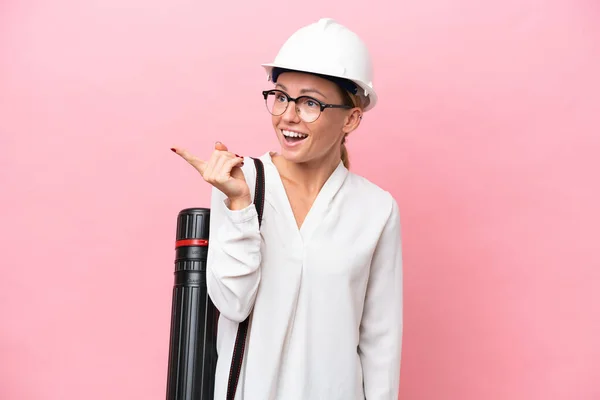 Young architect Russian woman with helmet and holding blueprints isolated on pink background intending to realizes the solution while lifting a finger up