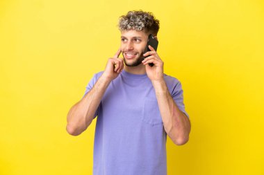 Young caucasian man using mobile phone isolated on yellow background thinking an idea while looking up