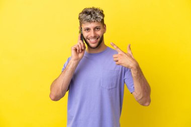 Sarı arka planda izole edilmiş cep telefonu kullanan beyaz bir adam işaret veriyor.