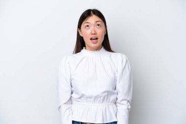 Beyaz arka planda izole edilmiş genç bir Çinli kadın yukarı bakıyor ve şaşırmış bir ifadeyle