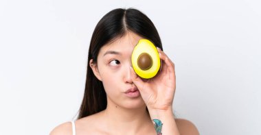 Beyaz arka planda avakado tutan genç Çinli bir kadın. Portreyi kapat