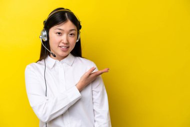 Sarı arka planda izole edilmiş kulaklıkla çalışan pazarlamacı Çinli kadın gülümseyerek bir fikir sunuyor.