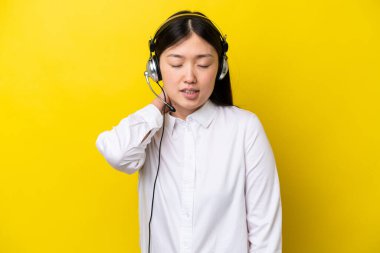 Telemarketer Çinli kadın kulaklıkla çalışıyor sarı arka planda, boyun ağrısı ile izole edilmiş.