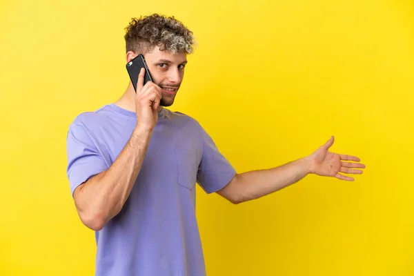 Jovem Caucasiano Usando Telefone Celular Isolado Fundo Amarelo Estendendo Mãos — Fotografia de Stock