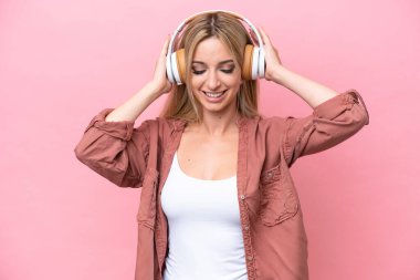 Güzel sarışın kadın pembe arka planda izole edilmiş müzik dinliyor.