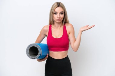 Genç spor sarışın kadın yoga derslerine giderken beyaz arka planda izole edilmiş bir minder tutuyor. Kuşkuları var ve el kaldırıyor.