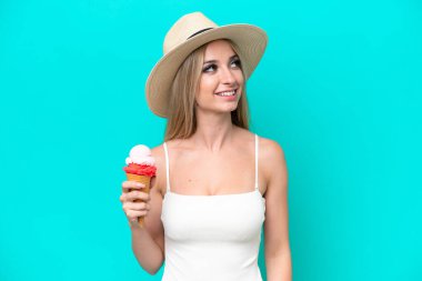 Mavi arka planda izole edilmiş dondurma tutan mayolu sarışın kadın gülümserken yukarı bakıyor.