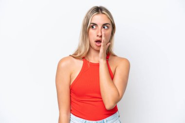 Beyaz arka planda izole edilmiş genç beyaz kadın yan tarafa bakarken sürpriz bir jest yaparak bir şeyler fısıldıyor.
