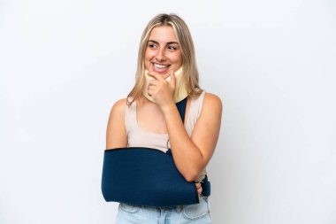 Kırık kollu ve askısı beyaz arka planda olan bir kadın yana bakıyor ve gülümsüyor.