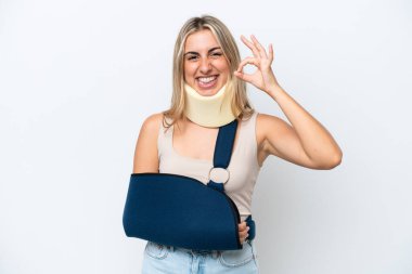 Kırık kollu ve beyaz arka planda askısı olan bir kadın parmaklarıyla işaret veriyor.