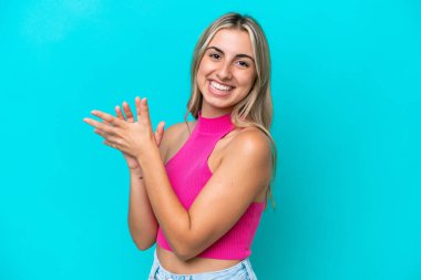 Mavi arka planda izole edilmiş genç beyaz kadın alkışlıyor.
