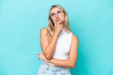 Kafkasyalı genç bir kadın mavi arka planda izole edilmiş. Şüpheleri var.