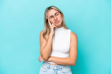 Kafkasyalı genç bir kadın mavi arka planda izole edilmiş, baş ağrısı var.