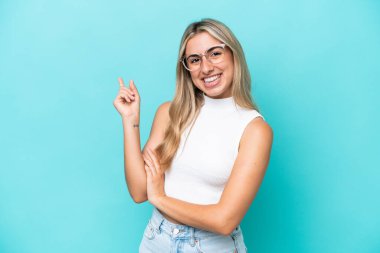 Mavi arka planda izole edilmiş genç beyaz kadın mutlu ve dik duruyor.
