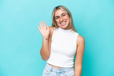 Mavi arka planda izole edilmiş beyaz bir kadın. Mutlu bir ifadeyle selamlıyor.