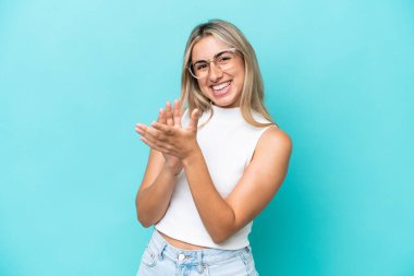 Mavi arka planda izole edilmiş genç beyaz kadın bir konferanstan sonra alkışlıyor.