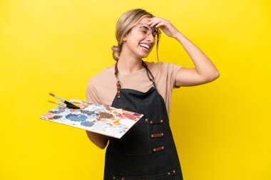 Sarı arka planda izole edilmiş palet tutan beyaz bir kadın kahkaha atıyor.