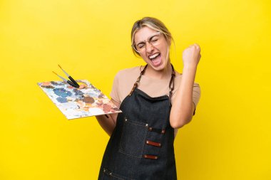 Sarı arka planda izole edilmiş palet tutan beyaz bir kadın zaferi kutluyor.